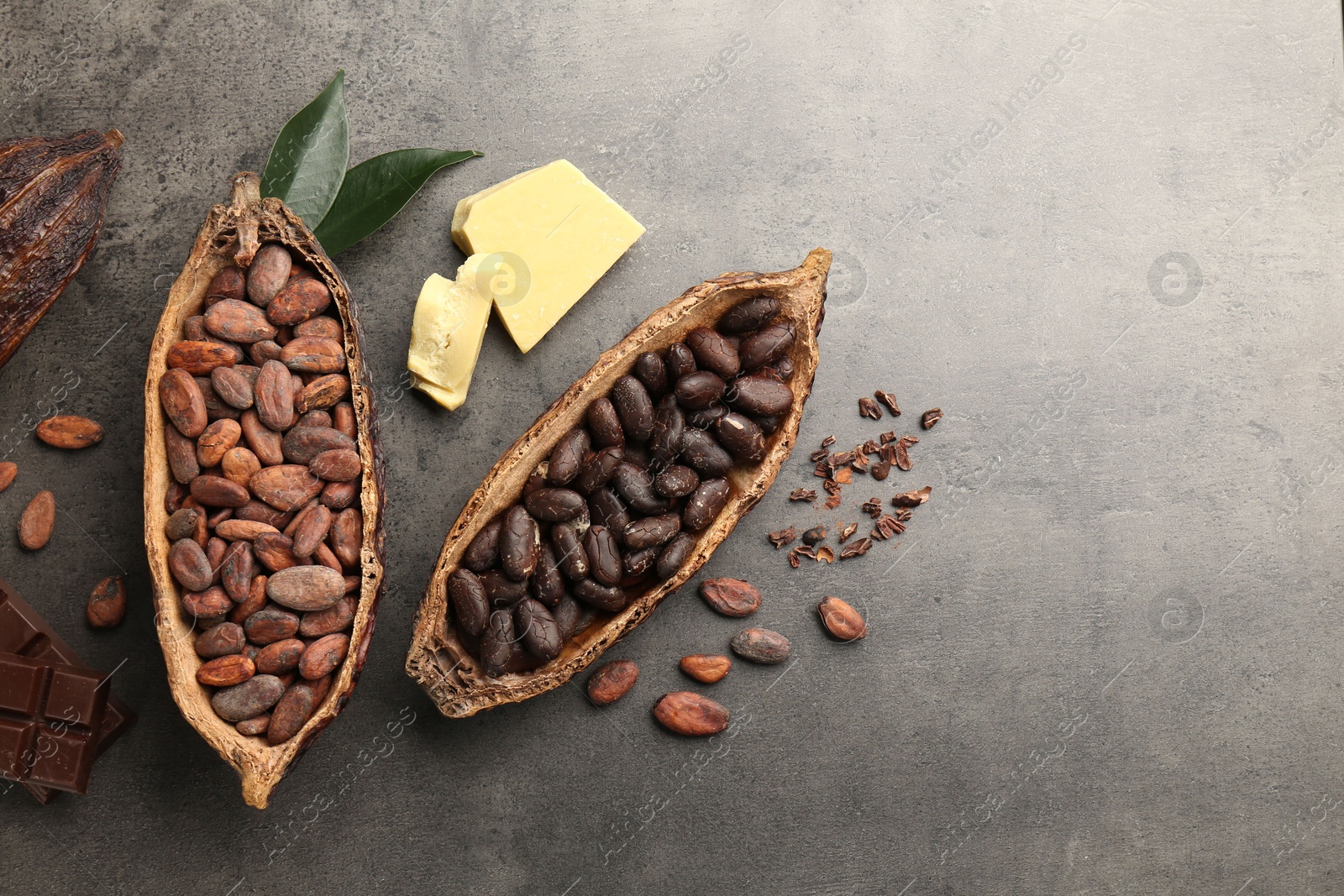 Photo of Cocoa pods with beans, chocolate, butter and leaves on grey background, flat lay. Space for text