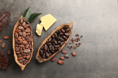 Cocoa pods with beans, chocolate, butter and leaves on grey background, flat lay. Space for text