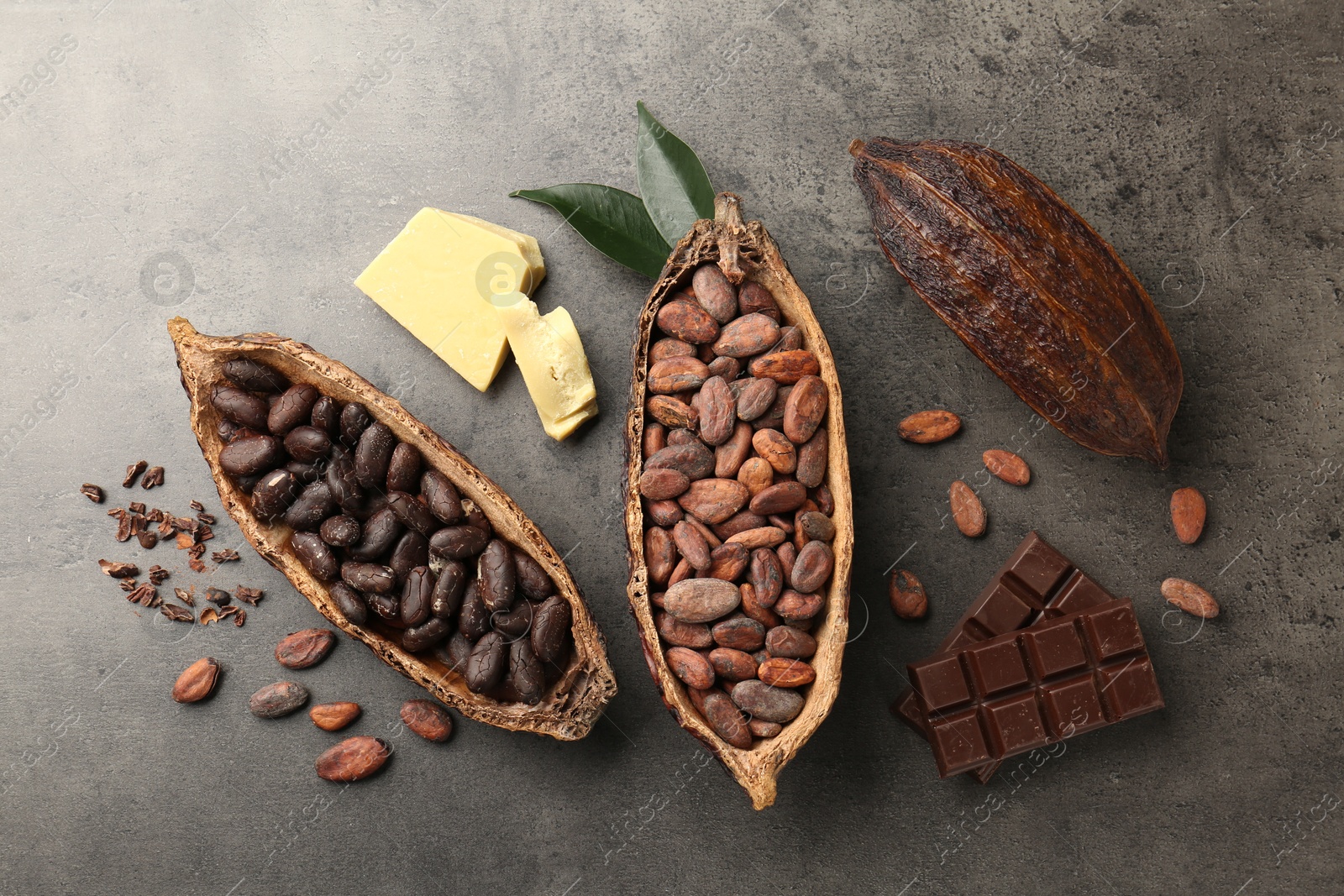 Photo of Cocoa pods with beans, chocolate, butter and leaves on grey background, flat lay