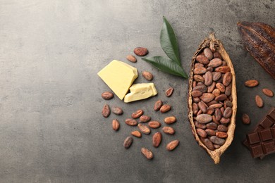 Cocoa pods with beans, chocolate, butter and leaves on grey background, flat lay. Space for text