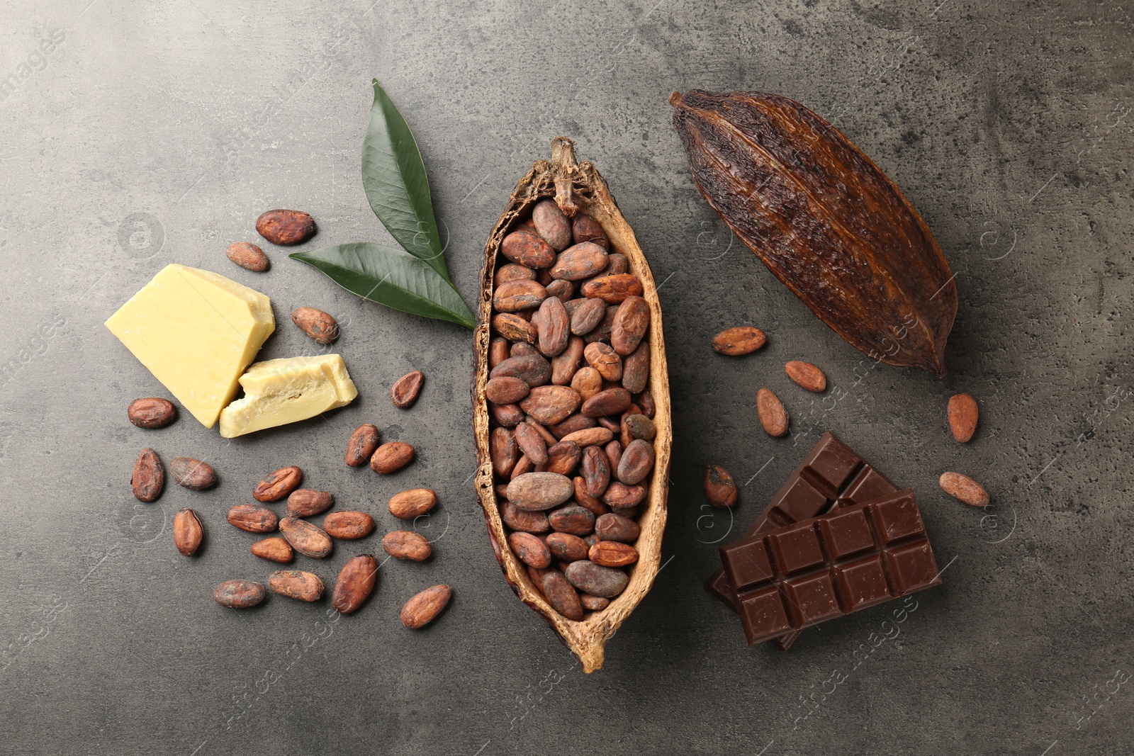 Photo of Cocoa pods with beans, chocolate, butter and leaves on grey background, flat lay