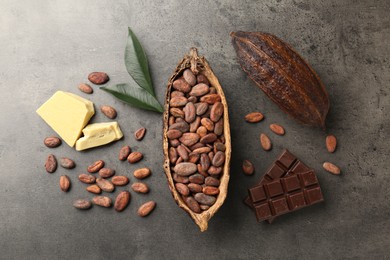 Cocoa pods with beans, chocolate, butter and leaves on grey background, flat lay