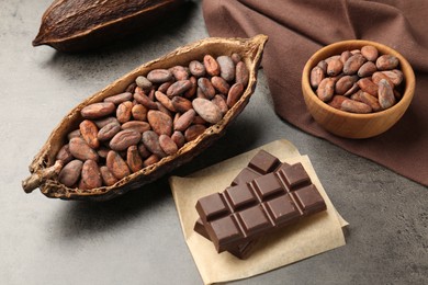 Photo of Cocoa pods with beans and chocolate on grey background, closeup