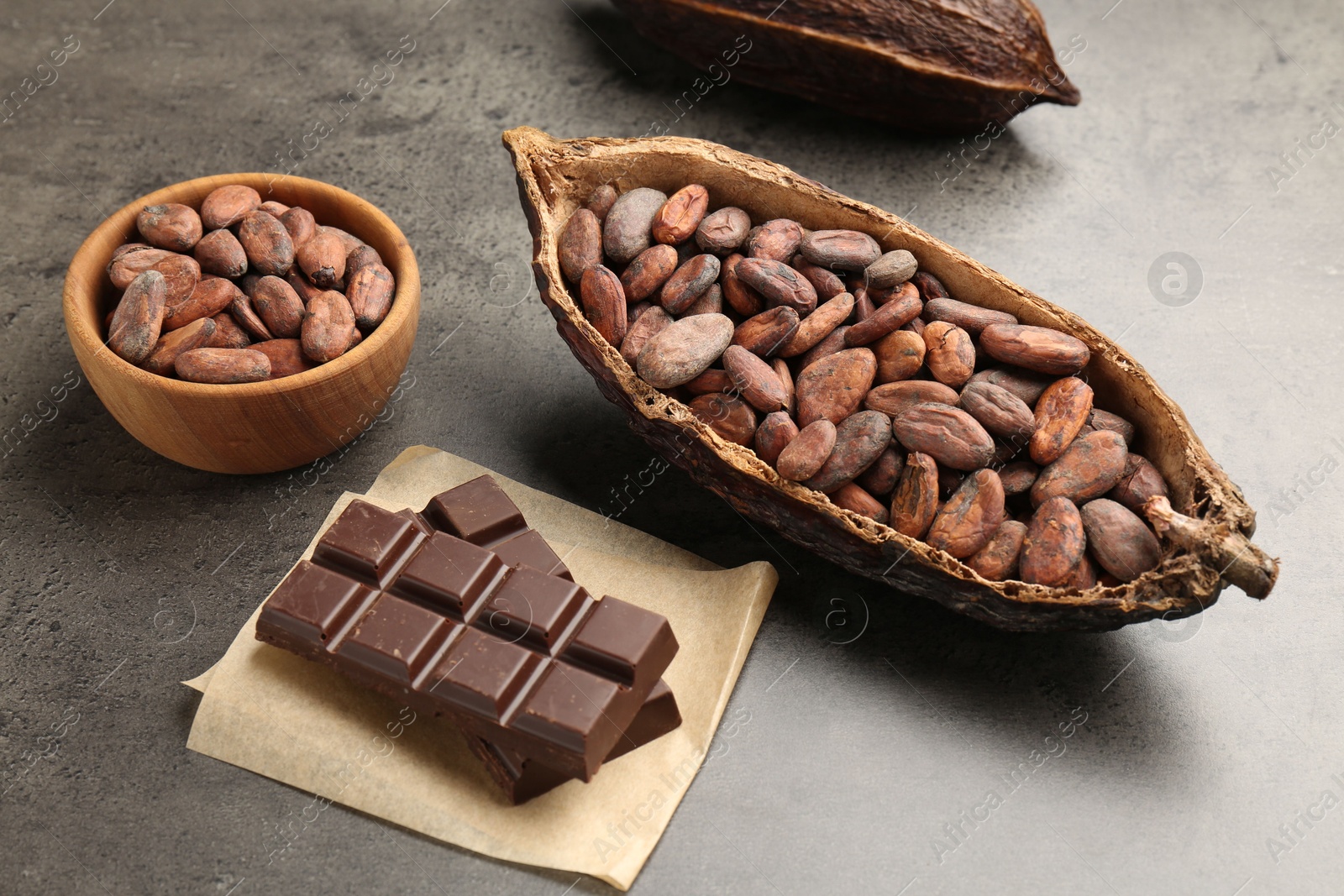 Photo of Cocoa pods with beans and chocolate on grey background, closeup