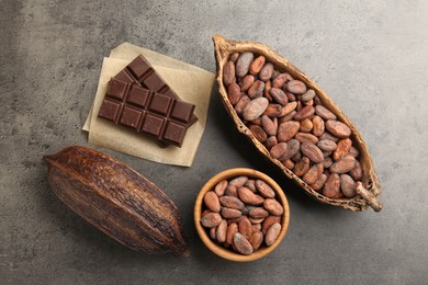 Cocoa pods with beans and chocolate on grey background, flat lay