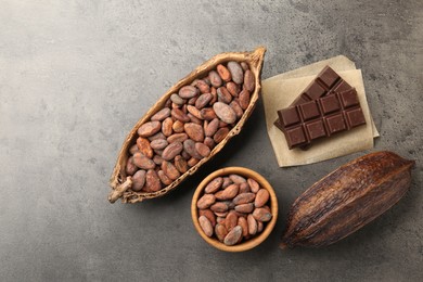 Cocoa pods with beans and chocolate on grey background, flat lay. Space for text