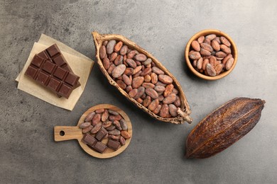 Cocoa pods with beans and chocolate on grey background, flat lay