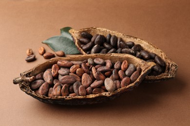 Cocoa pods with beans and leaves on brown background, closeup