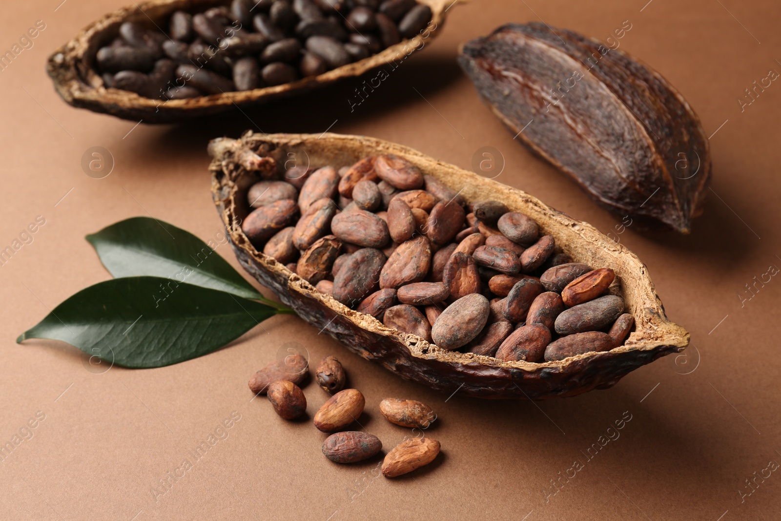 Photo of Cocoa pods with beans and leaves on brown background, closeup