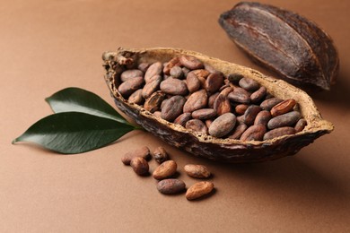 Photo of Cocoa pods with beans and leaves on brown background, closeup