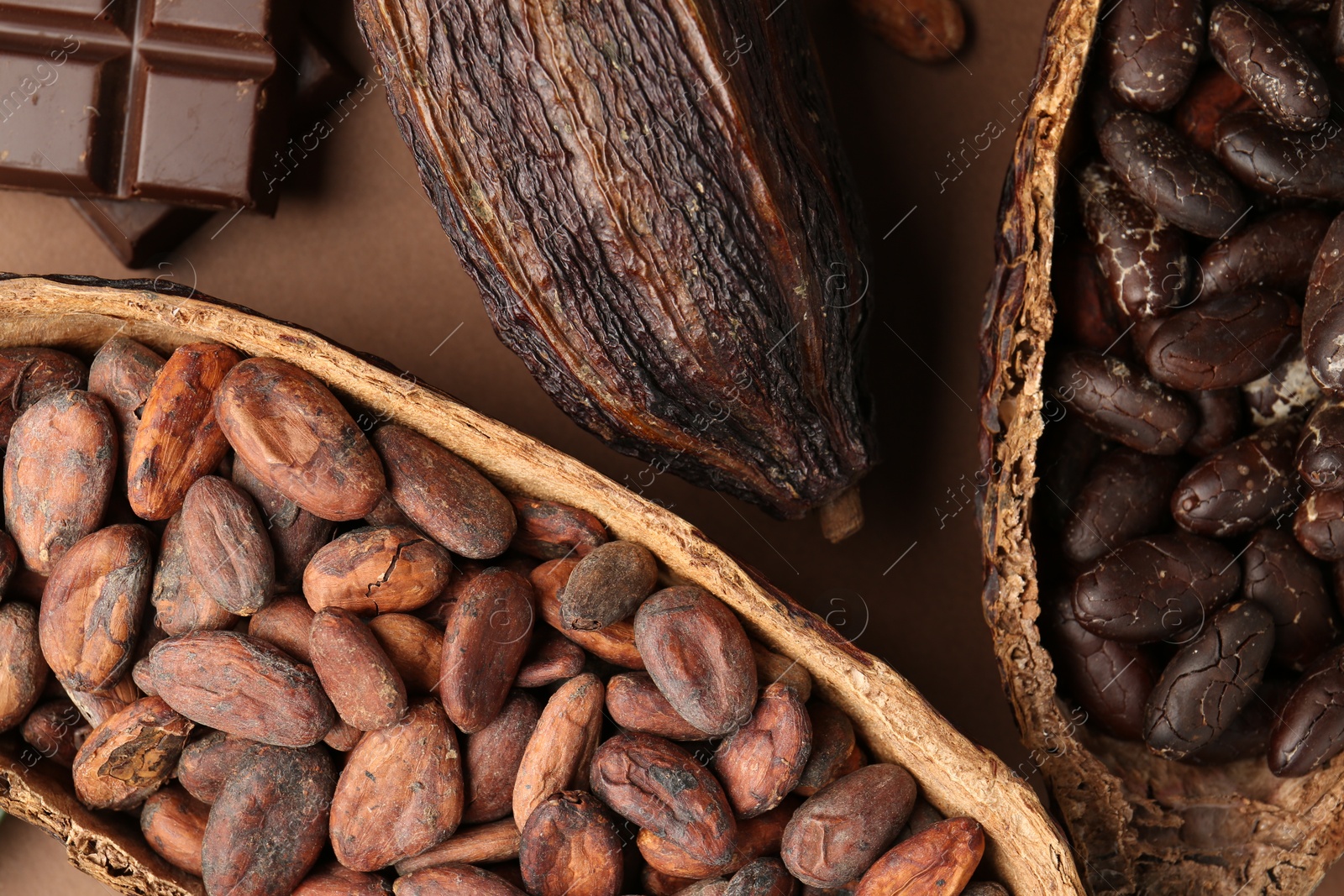 Photo of Cocoa pods with beans and chocolate on brown background, flat lay