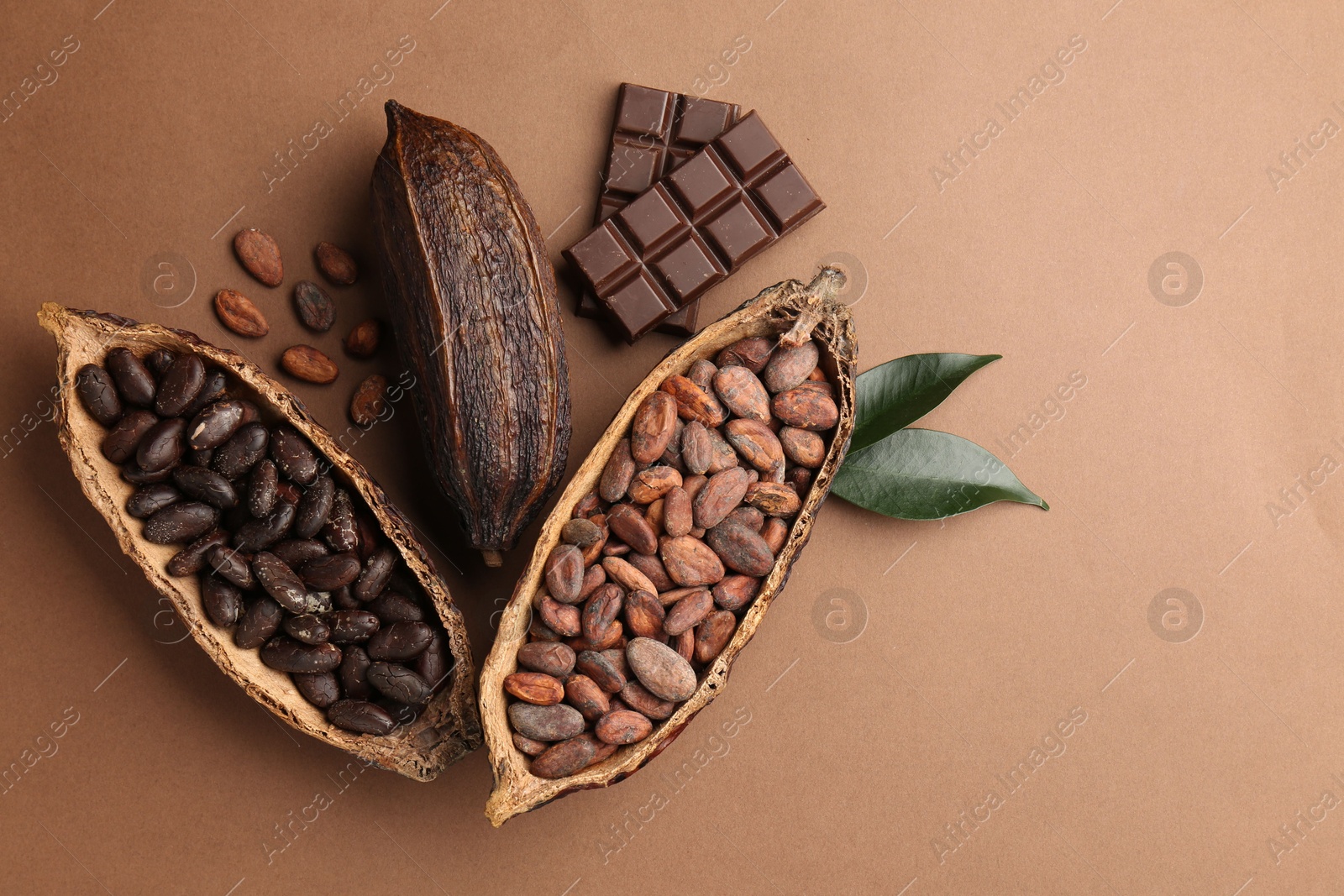 Photo of Cocoa pods with beans, chocolate and leaves on brown background, flat lay