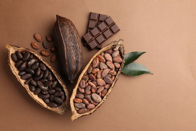 Cocoa pods with beans, chocolate and leaves on brown background, flat lay