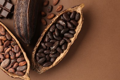 Cocoa pods with beans and chocolate on brown background, flat lay