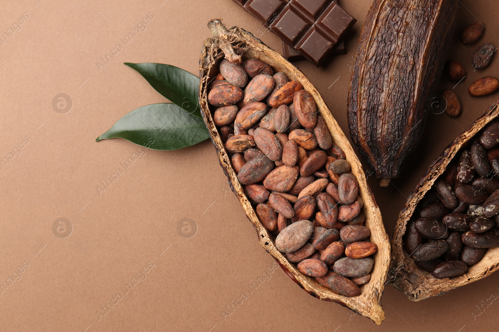 Photo of Cocoa pods with beans, chocolate and leaves on brown background, flat lay