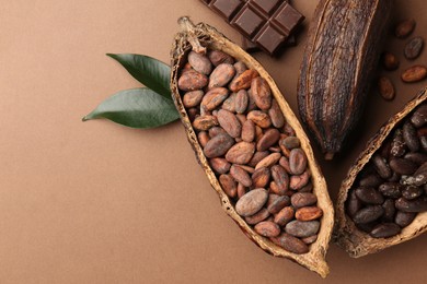 Cocoa pods with beans, chocolate and leaves on brown background, flat lay