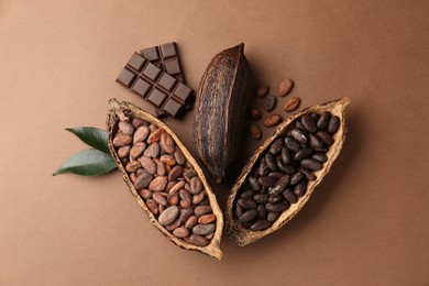 Photo of Cocoa pods with beans, chocolate and leaves on brown background, flat lay