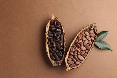 Cocoa pods with beans and leaves on brown background, flat lay. Space for text