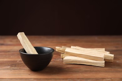 Photo of Palo santo sticks on wooden table against dark background, closeup