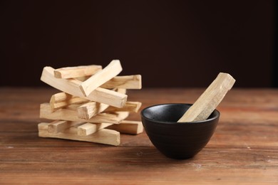 Photo of Palo santo sticks on wooden table against dark background, closeup