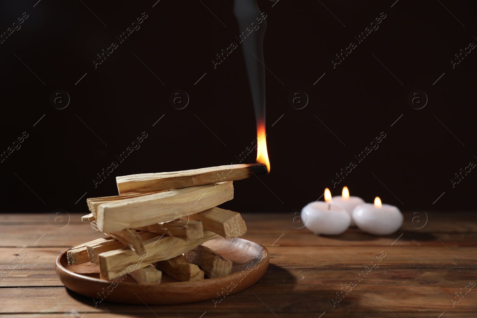 Photo of Palo santo sticks and burning one on wooden table against black background, closeup