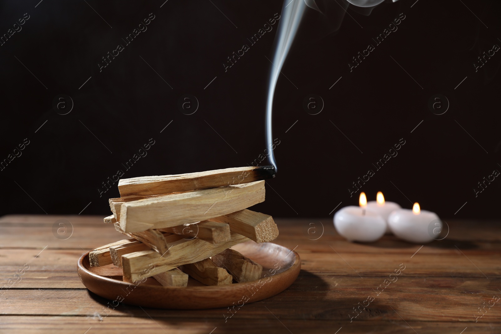 Photo of Palo santo sticks and smoldering one on wooden table against black background, closeup