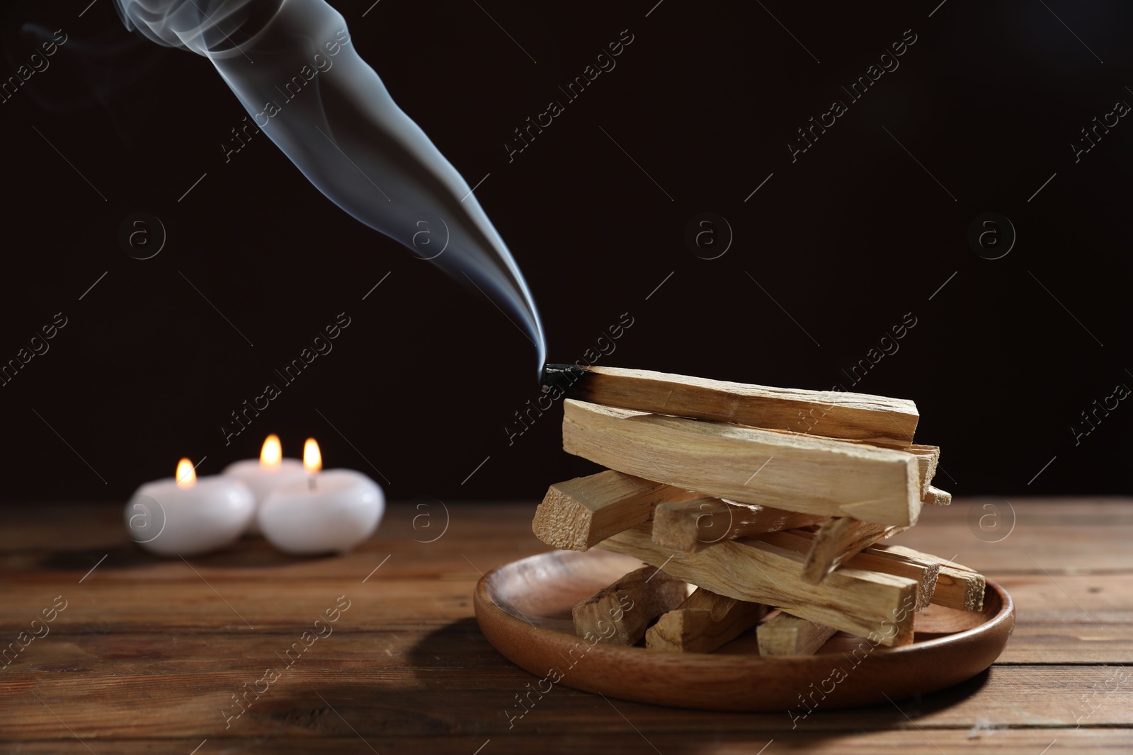 Photo of Palo santo sticks and smoldering one on wooden table against black background, closeup