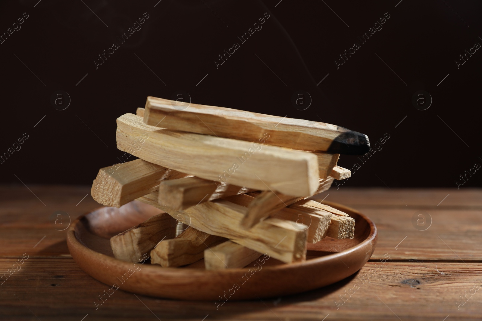 Photo of Palo santo sticks and burnt one on wooden table against black background, closeup