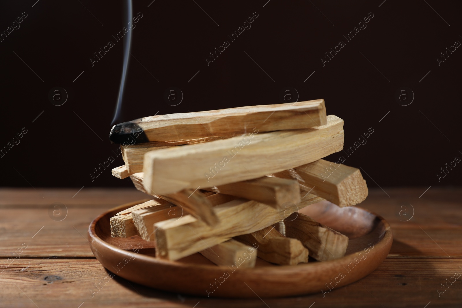 Photo of Palo santo sticks and smoldering one on wooden table against black background, closeup