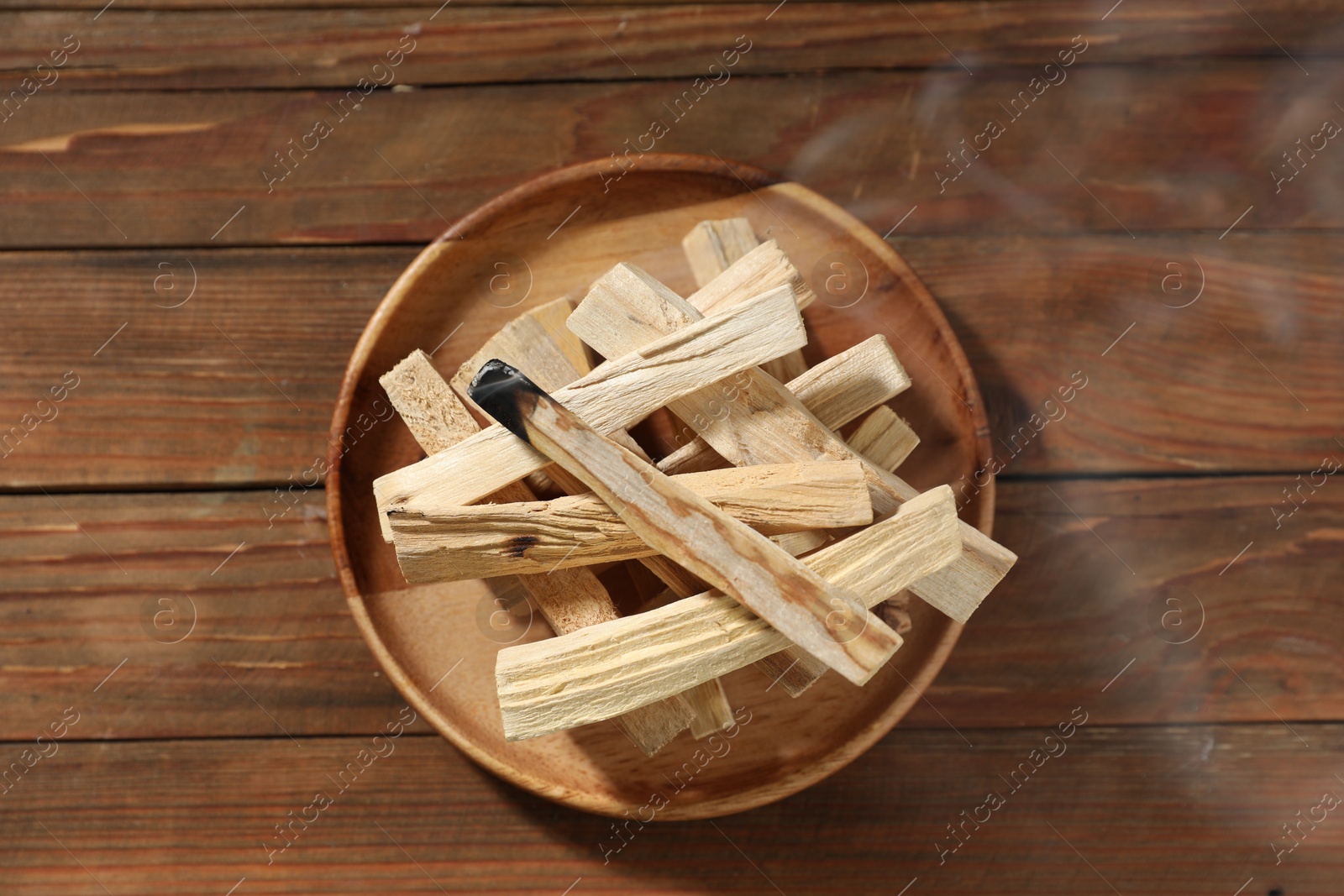 Photo of Palo santo sticks and smoldering one on wooden table, top view