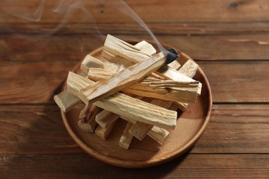 Photo of Palo santo sticks and smoldering one on wooden table, closeup