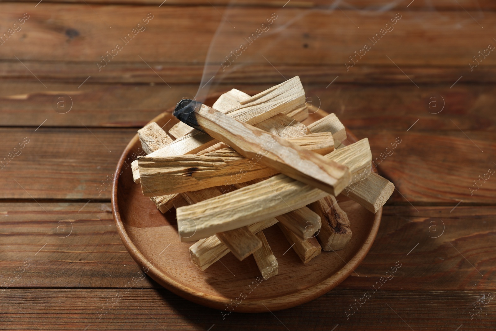 Photo of Palo santo sticks and smoldering one on wooden table, closeup