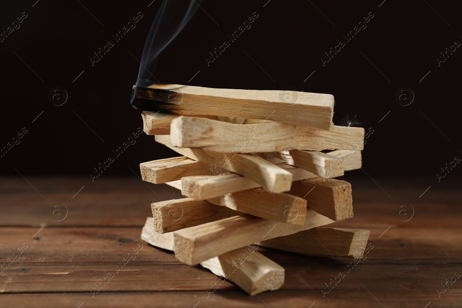 Photo of Palo santo sticks and smoldering one on wooden table against black background, closeup