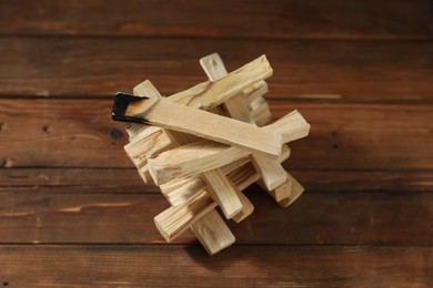 Photo of Palo santo sticks and burnt one on wooden table, closeup