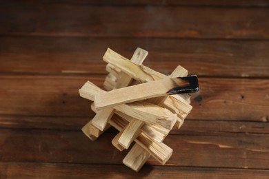 Photo of Palo santo sticks and smoldering one on wooden table, closeup