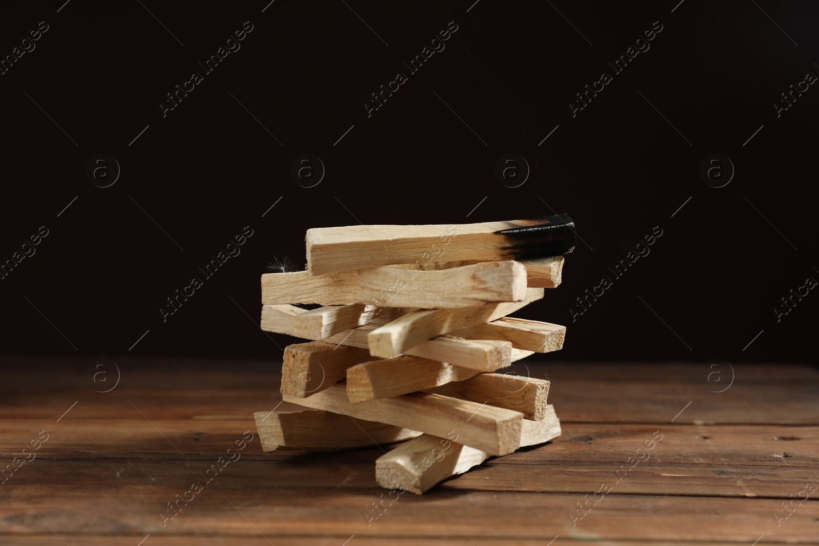 Photo of Palo santo sticks and burnt one on wooden table against black background, closeup