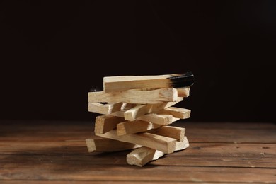 Photo of Palo santo sticks and burnt one on wooden table against black background, closeup