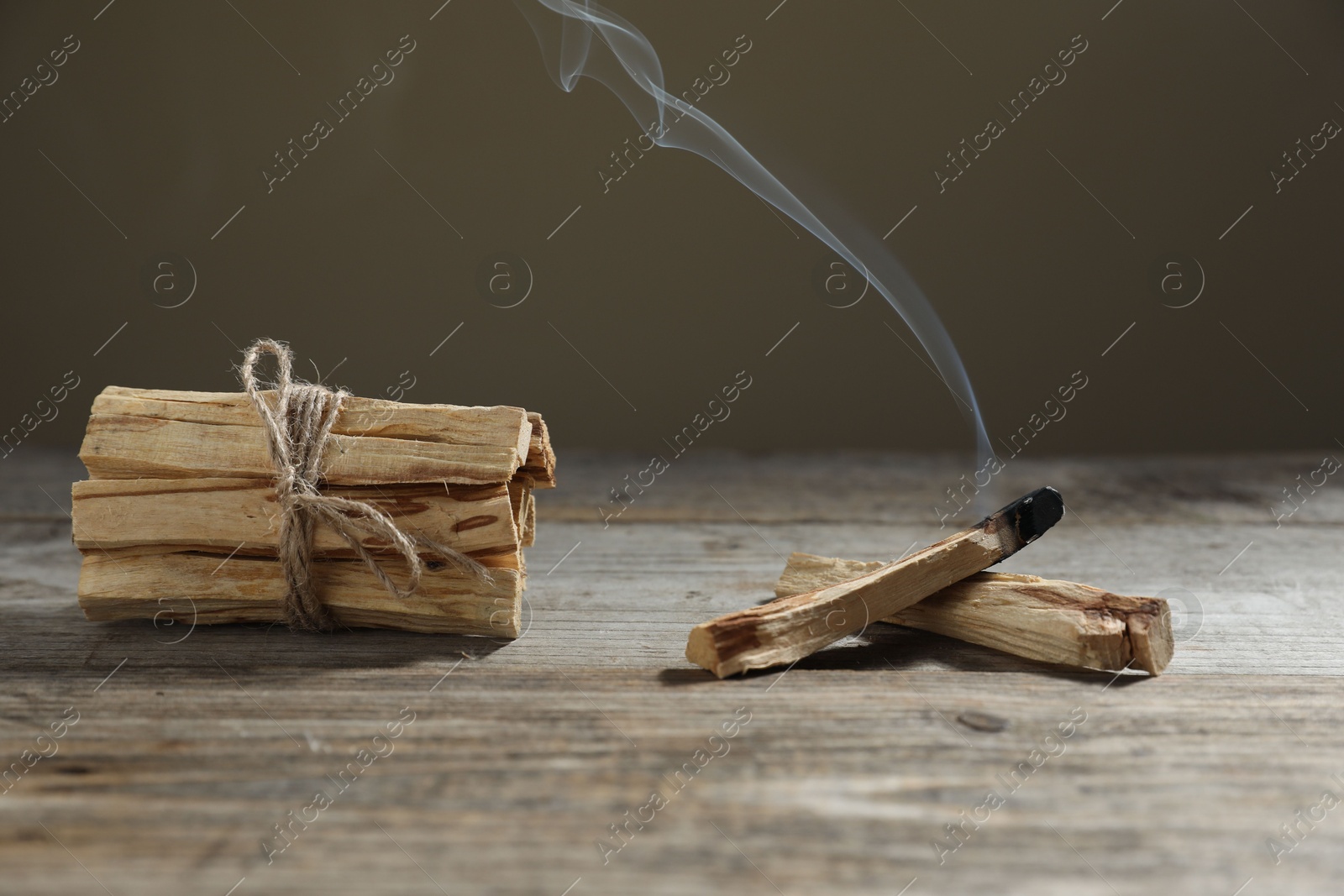 Photo of Palo santo sticks and smoldering one on wooden table against grey background, closeup