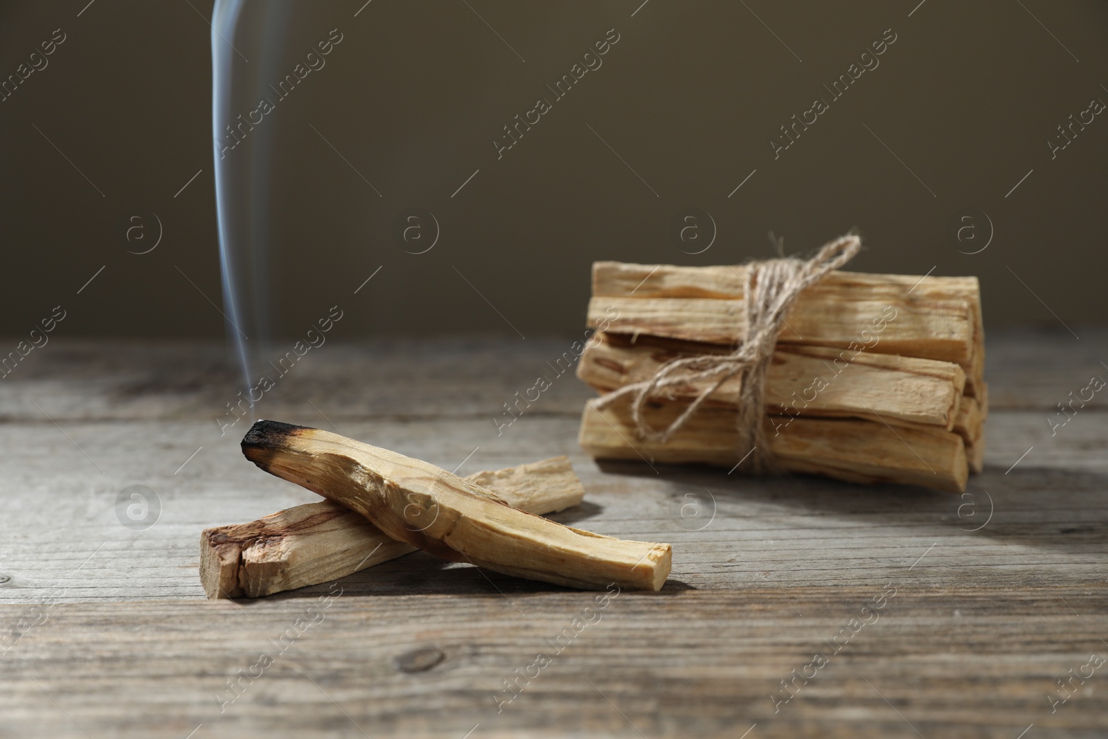 Photo of Palo santo sticks and smoldering one on wooden table against grey background, closeup