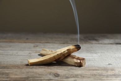 Photo of Palo santo sticks and smoldering one on wooden table against grey background, closeup