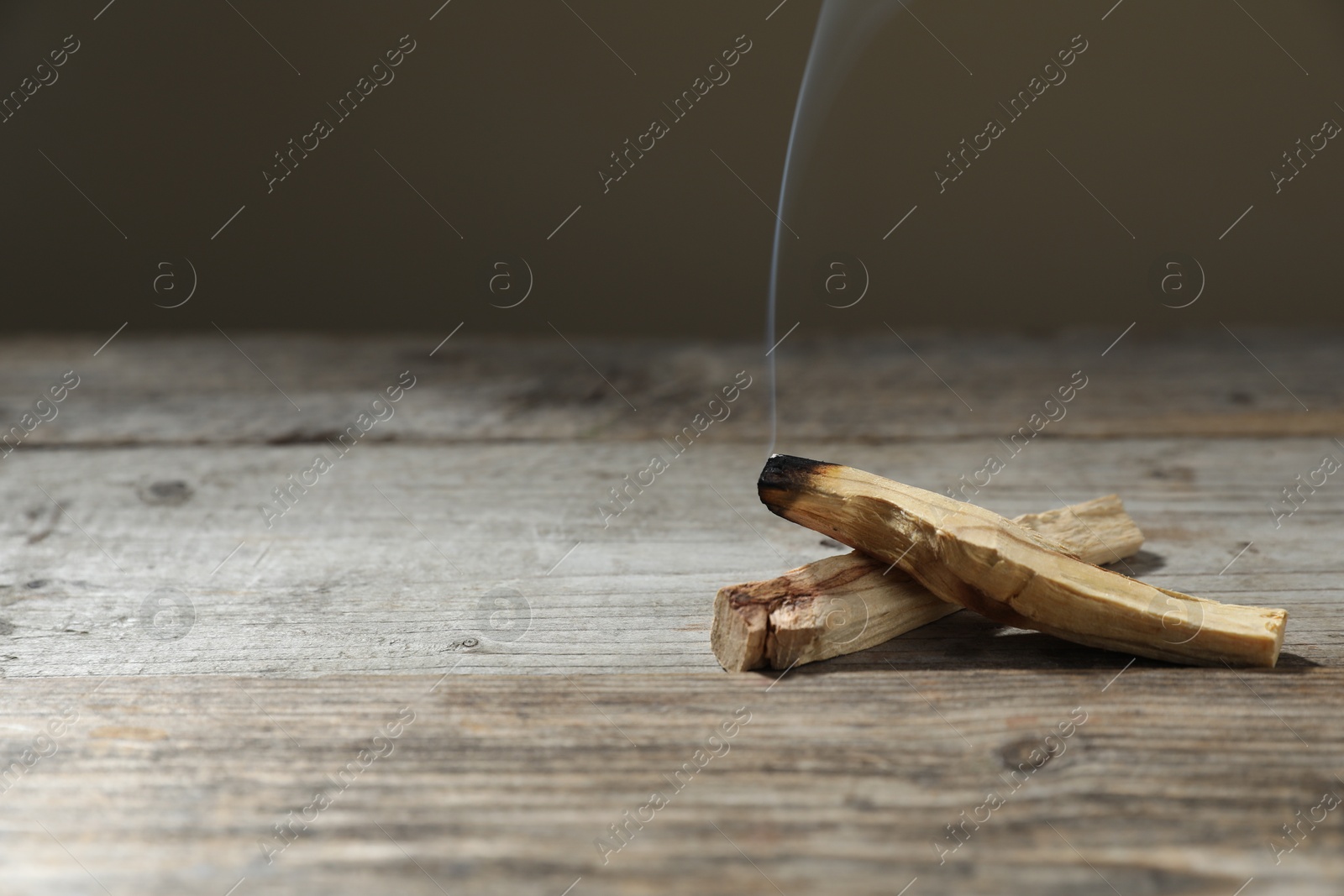 Photo of Palo santo sticks and smoldering one on wooden table against grey background, closeup. Space for text