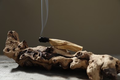 Photo of Smoldering palo santo stick and snag on wooden table against grey background, closeup