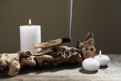 Photo of Smoldering palo santo stick, burning candles and snag on wooden table against grey background, closeup