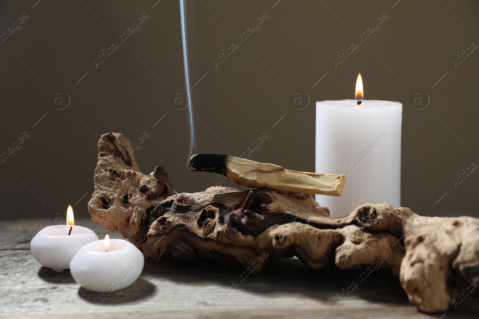 Photo of Smoldering palo santo stick, burning candles and snag on wooden table against grey background, closeup