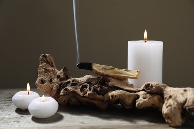 Photo of Smoldering palo santo stick, burning candles and snag on wooden table against grey background, closeup