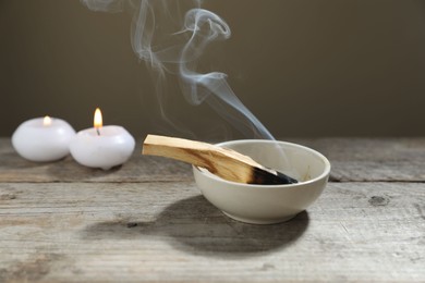 Photo of Smoldering palo santo stick and burning candles on wooden table against grey background, closeup