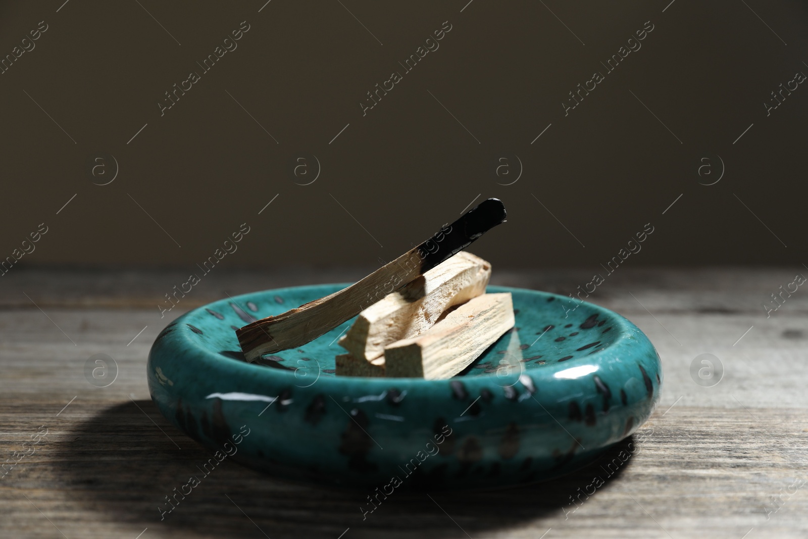 Photo of Palo santo sticks and burnt one on wooden table against grey background, closeup