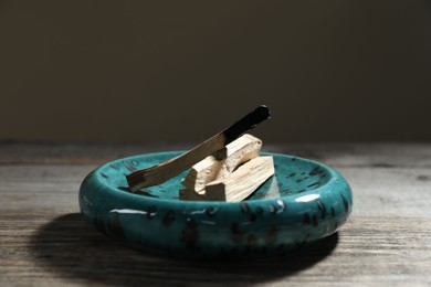 Photo of Palo santo sticks and burnt one on wooden table against grey background, closeup