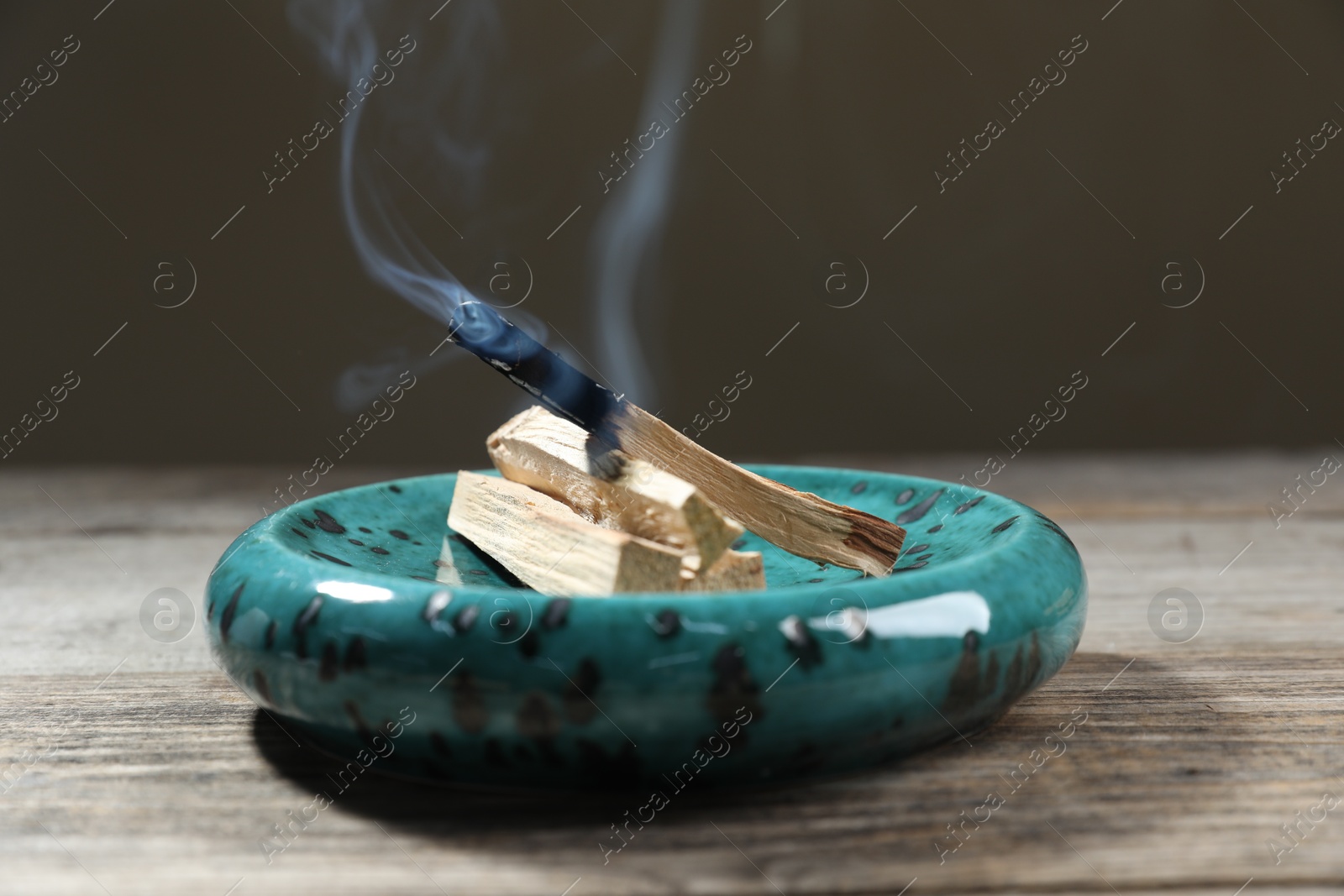 Photo of Palo santo sticks and smoldering one on wooden table against grey background, closeup