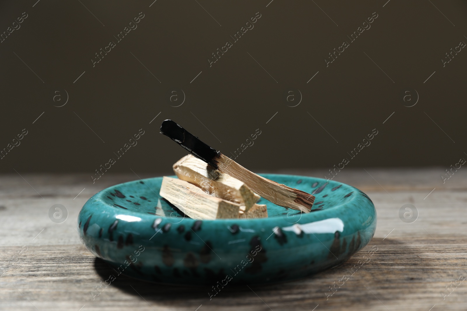 Photo of Palo santo sticks and burnt one on wooden table against grey background, closeup